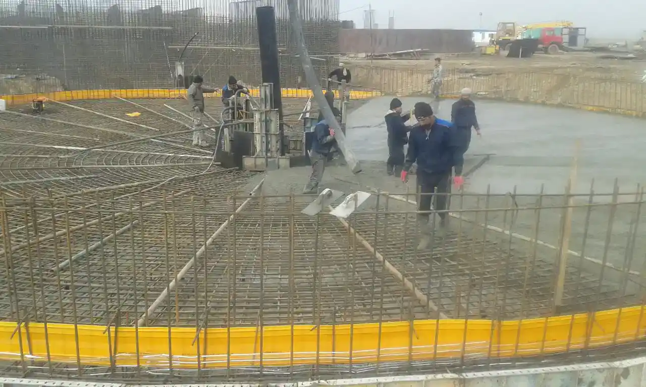 Workers smoothing circular concrete base with reinforcement – treatment tank foundation