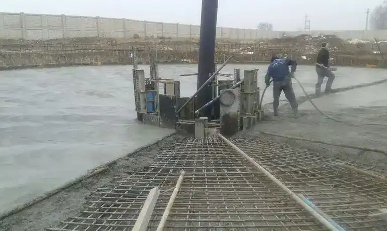 Workers pouring and leveling concrete over a rebar-reinforced circular base with central formwork – Zarnam wastewater treatment plant construction